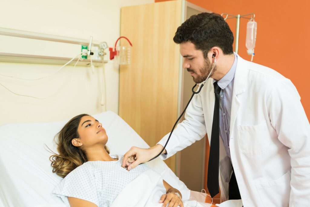 Doctor using a stethoscope to examine a patient lying in a hospital bed during a routine medical evaluation.