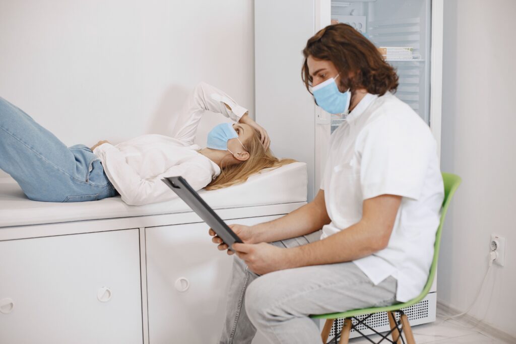 Healthcare provider reviewing patient information while consulting with a patient lying on an examination table in a medical clinic.