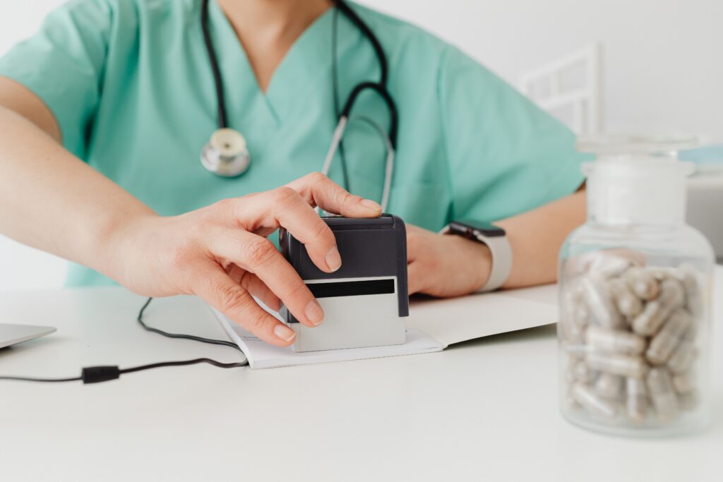 Healthcare professional stamping medical documents at a clinic desk with prescription medication in the background.