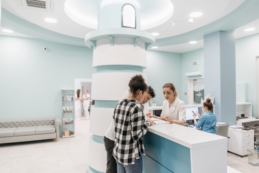 Patients checking in at the reception desk of a modern medical clinic with healthcare staff providing assistance.